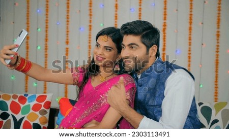 Indian couple happily posing while capturing selfies during the festive season. Attractive newly wedded husband-wife clicking pictures in traditional clothing - Diwali celebration