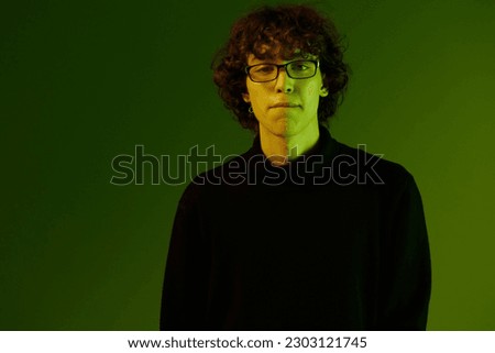 Young male portrait close-up in glasses fashion and style, hipster lifestyle, portrait green background mixed neon light, copy space