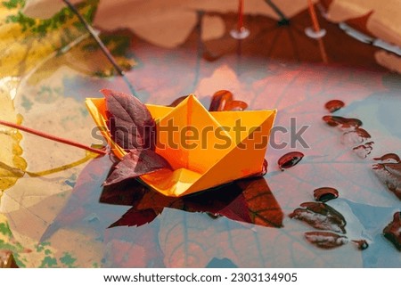 Origami paper yellow boat and scenic fallen leaves in water. Concept of bright fall