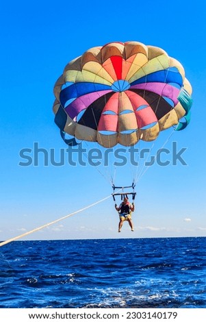 Parasailing water amusement - flying on a parachute behind a boat on a summer holiday by the sea. Summer vacation concept Royalty-Free Stock Photo #2303140179