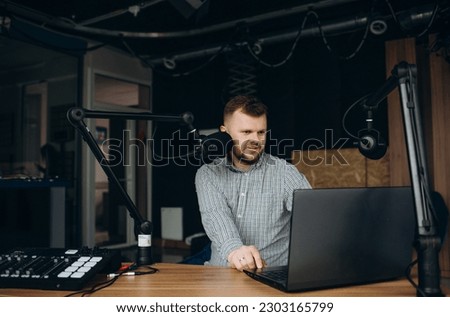 Portrait of a successful African American influencer, man smiling and looking at the camera, using a laptop and a professional microphone at work to record podcasts and read audio books online.