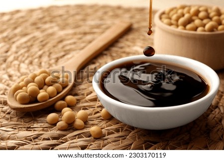 Soy sauce drops falling into bowl on wicker mat, closeup Royalty-Free Stock Photo #2303170119