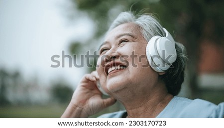 Mature Asian woman in wheelchair has relax time in park, she listening music frome headphone, smile with happy, copy space for insert your advertising