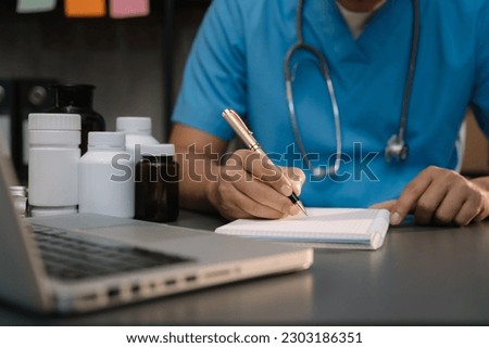 Male medical doctor's hands write a note and use laptop working. Doctor's working place. Healthcare and medical concept.