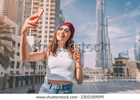 happy tourist asian girl taking selfie photos for her travel blog, in Dubai downtown district against background of the grandiose Burj Khalifa highest skyscraper in the world