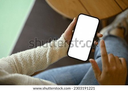 Close-up image of a woman in cozy white sweater using her smartphone while relaxing in a coffee shop. Lifestyle and technology concept