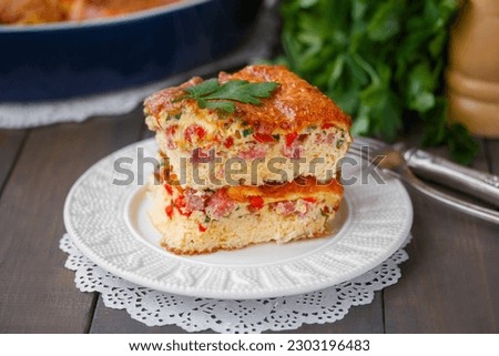 Fluffy Oven Baked omelette with cheese, tomato and ham sliced on a white ceramic plate. Vegetable Soufflé or Puffy omelet. Selective focus, horizontal, closeup, wooden table. Royalty-Free Stock Photo #2303196483