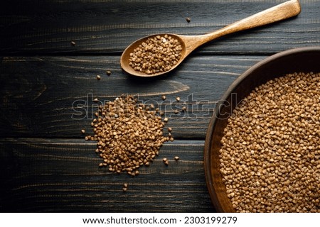 A plate of buckwheat groats and sprinkles near a spoon on a vintage table before cooking. Place for recipe or menu on black background Royalty-Free Stock Photo #2303199279