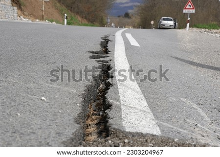 Asphalt road with long cracks caused by erosion or earthquake. Damaged paved road, restricted movement to one lane on the mountain