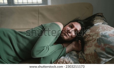 One young Middle Eastern woman laying on couch resting and relaxing. An Arab adult girl feeling unwinding Royalty-Free Stock Photo #2303211173