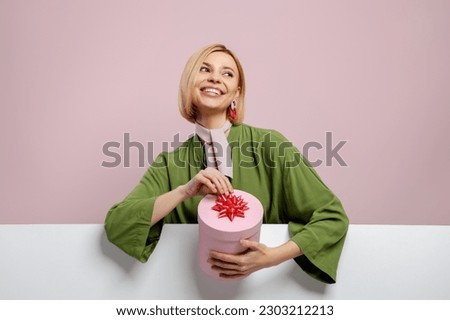 Attractive young woman holding a gift box and smiling against pink background