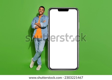 Full body photo of positive confident male lean on huge display screen smartphone isolated on green color background