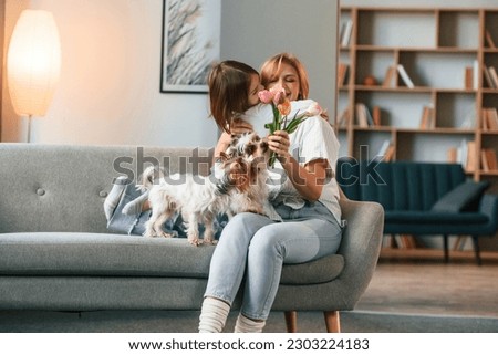 With flowers. Mother with her daughter and with two cute dogs is in domestic room. Royalty-Free Stock Photo #2303224183