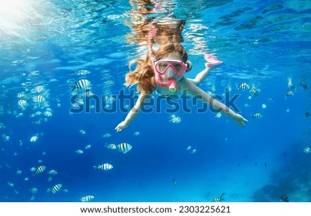 A little girl with mask and snorkel enjoys the underwater life of the tropical ocean wth colorful fishes in the Maldives Royalty-Free Stock Photo #2303225621