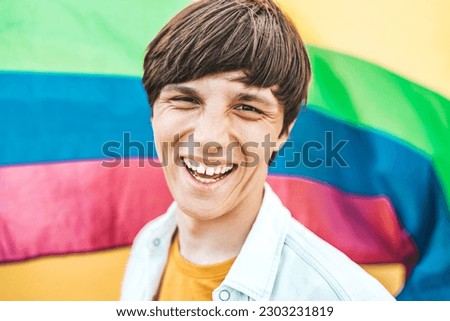 Gay man with rainbow flag smiling at camera - Lgbt pride concept with cheerful homosexual guy laughing outside