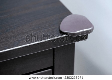 Corner bumper guard at black wooden cabinet angle. Protect children from sharp part of furniture.