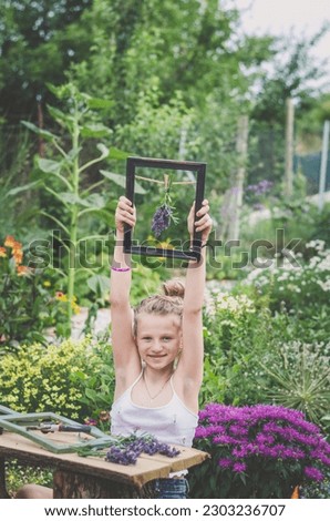 adorable happy smiling blond girl sitting in the garden and creating lavender framed images