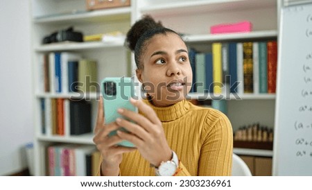 Young african american woman student using smartphone at the library
