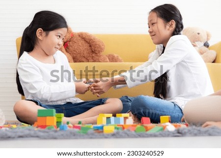 Naughty girl play block game and snatch toy from her sister. Asian kids have fun family leisure activity together playing and funny fighting at home. Female child pulling snatching with her sibling. Royalty-Free Stock Photo #2303240529