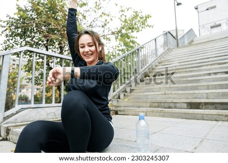 Young athlete woman checking her fitness tracker and celebrating success. Heart rate, smartwatch and running with young woman in city for cardio, progress and goal tracker Royalty-Free Stock Photo #2303245307