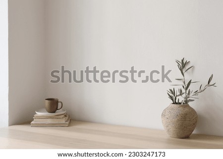 Neutral Mediterranean home design. Textured vase with olive tree branches, cup of coffee. Books on wooden table. Living room still life. Empty wall copy space. Modern interior, no people. Lateral view Royalty-Free Stock Photo #2303247173