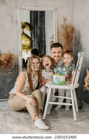 Mother, father hugging kids. Birthday reception. Mom, dad, daughter congratulate son on birthday near grey wall in studio. Happy family with cake and having fun celebrating a birthday party 2 years.