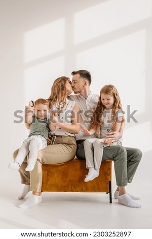 Parents hugs children relaxing on sofa on wall at home. Family moving into new house, feeling joy. Young happy mother kisses father, embrace child daughter and son isolated on white background studio.