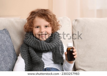 Cute boy holding bottle with cough syrup on sofa indoors. Effective medicine Royalty-Free Stock Photo #2303257983