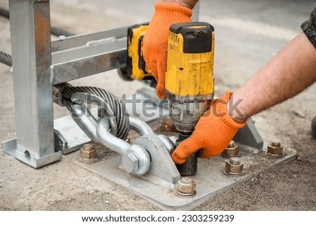 Tightening of bolts nuts screw washer in concrete surface. Cable tensioning. Installation of support in crash barriers on highway. Bridge construction. Metal road fencing on freeway. Road guard rails. Royalty-Free Stock Photo #2303259239