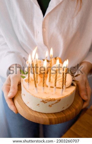 A festive cake with beautiful decorations and burning candles in a woman's hands. Vertical Shot.