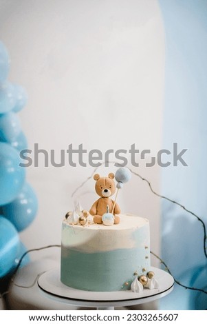 Trendy cake with a figure bear decorated gold decor for a boy. Baby shower. Celebration baptism concept. Delicious reception at a birthday party. Birthday cake on a background blue balloons. Closeup.