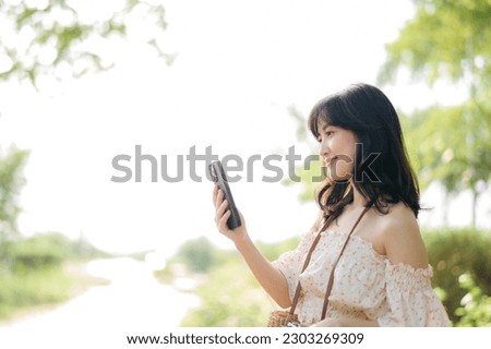 Portrait of young asian woman traveler with weaving hat, basket, mobile phone and camera on green public park background. Journey trip lifestyle, world travel explorer or Asia summer tourism concept.