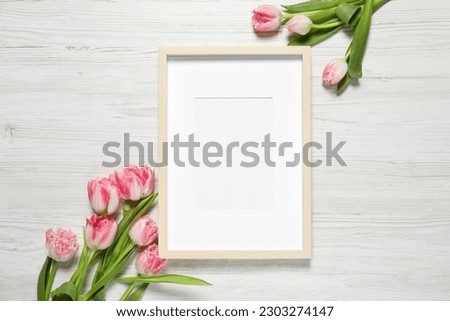Empty photo frame and beautiful flowers on white wooden table, flat lay. Space for design