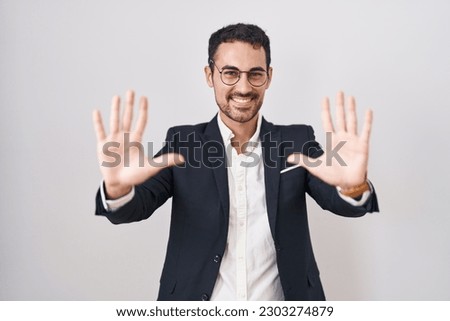 Handsome business hispanic man standing over white background showing and pointing up with fingers number ten while smiling confident and happy. 