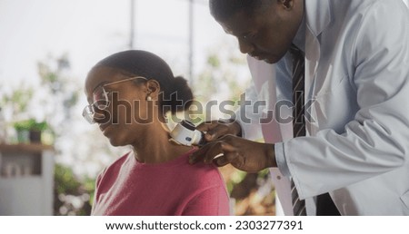 African Skin Care Professional Using a Dermatoscope to Examine Neck Tissue on the Skin of an Attractive Young Black Female During a Health Check Visit to a Clinic Royalty-Free Stock Photo #2303277391