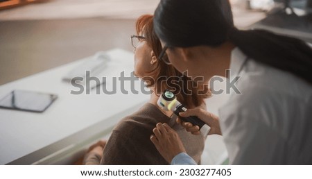 Young Asian Dermatologist is Using a Dermatoscope to Identify Worrying Cancerogenic Tissues on the Skin of a Senior Female During a Health Check Visit to a Clinic. Female Doctor Working in Hospital Royalty-Free Stock Photo #2303277405