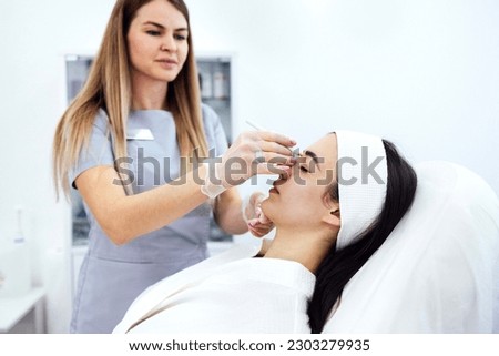 Beauty injections. Female cosmetologist in transparent gloves makes an injection in the lower jaw of her client. Treatment with hyaluronic acid. Introduction of liquid into the skin of woman. Royalty-Free Stock Photo #2303279935