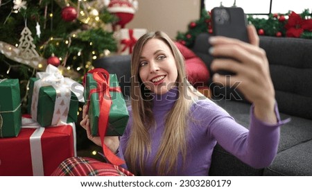 Young blonde woman make selfie by smartphone sitting on floor by christmas tree at home