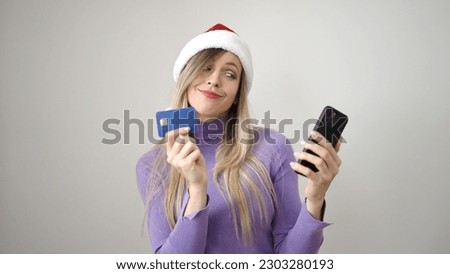 Young blonde woman wearing christmas hat using smartphone and credit card over isolated white background