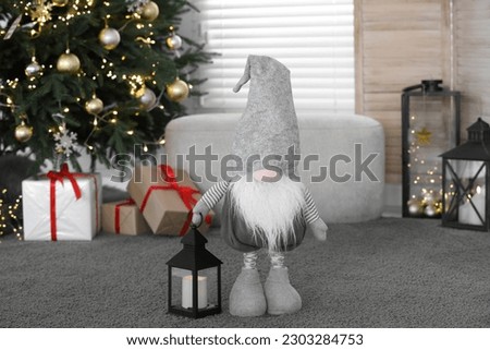Cute Scandinavian gnome with lantern candle holder near Christmas tree on carpet in room