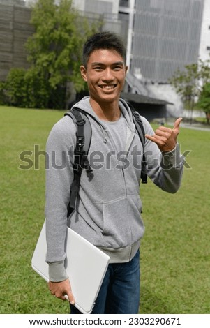 Portrait of handsome male student ,standing  with  holding laptop with backpack, in outdoors on campus of university