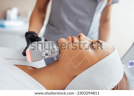 Portrait of relaxed young female client getting SMAS ultrasound face lifting massage with professional equipment in beauty center