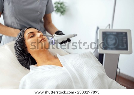 Microneedle RF lifting procedure. Hardware cosmetology. Beautician conducts a facial rejuvenation procedure for a brunette woman Royalty-Free Stock Photo #2303297893