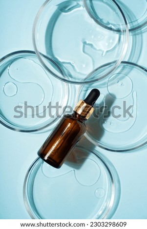 Cosmetic beauty concept with bottle serum, drops and petri dish on blue background, top view, flat lay, vertical