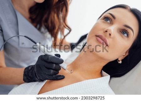 Beautiful caucasian young woman is doing a mole removal procedure in a modern beauty cosmetic dermatological clinic. Skin moles treatment by laser method. Close up. Free space for text Royalty-Free Stock Photo #2303298725