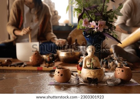 Selective focus, close-up of a statuette representing pachamama, in the background out of focus a woman and a man playing sound therapy instruments. Sound therapy instruments.