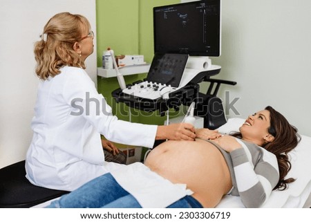 Female doctor doing ultrasound scan for a beautiful pregnant woman. Side view. Modern pregnancy  and healthcare concept. Royalty-Free Stock Photo #2303306719