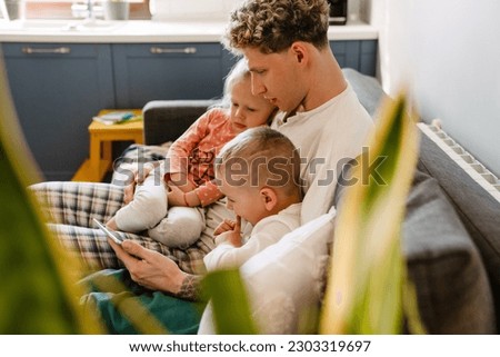 Young father and his children wearing pajamas watching cartoons on digital tablet while sitting on couch at home