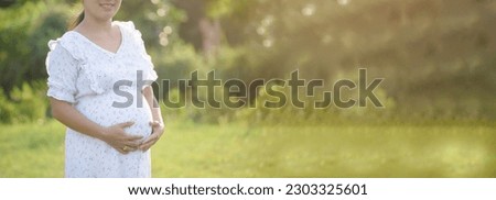 Late Pregnant woman stand and rub and touch her belly in the park-Banner image