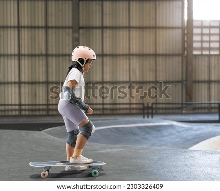 asian child skater or kid girl fun playing skateboard or start ride surf skate in indoor pump track skate park by extreme sports surfing to wears helmet elbow pads wrist knee guard for body safety Royalty-Free Stock Photo #2303326409